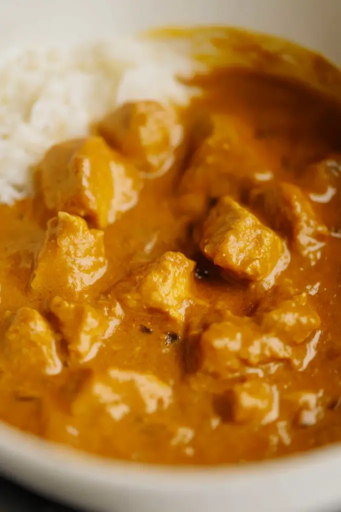 Close-up of golden chicken pieces simmering in pumpkin coconut sauce